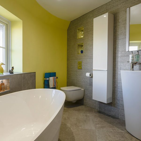 Colourful yellow bathroom with a grey feature wall and white appliances by Bathroom Inspirations Dorchester